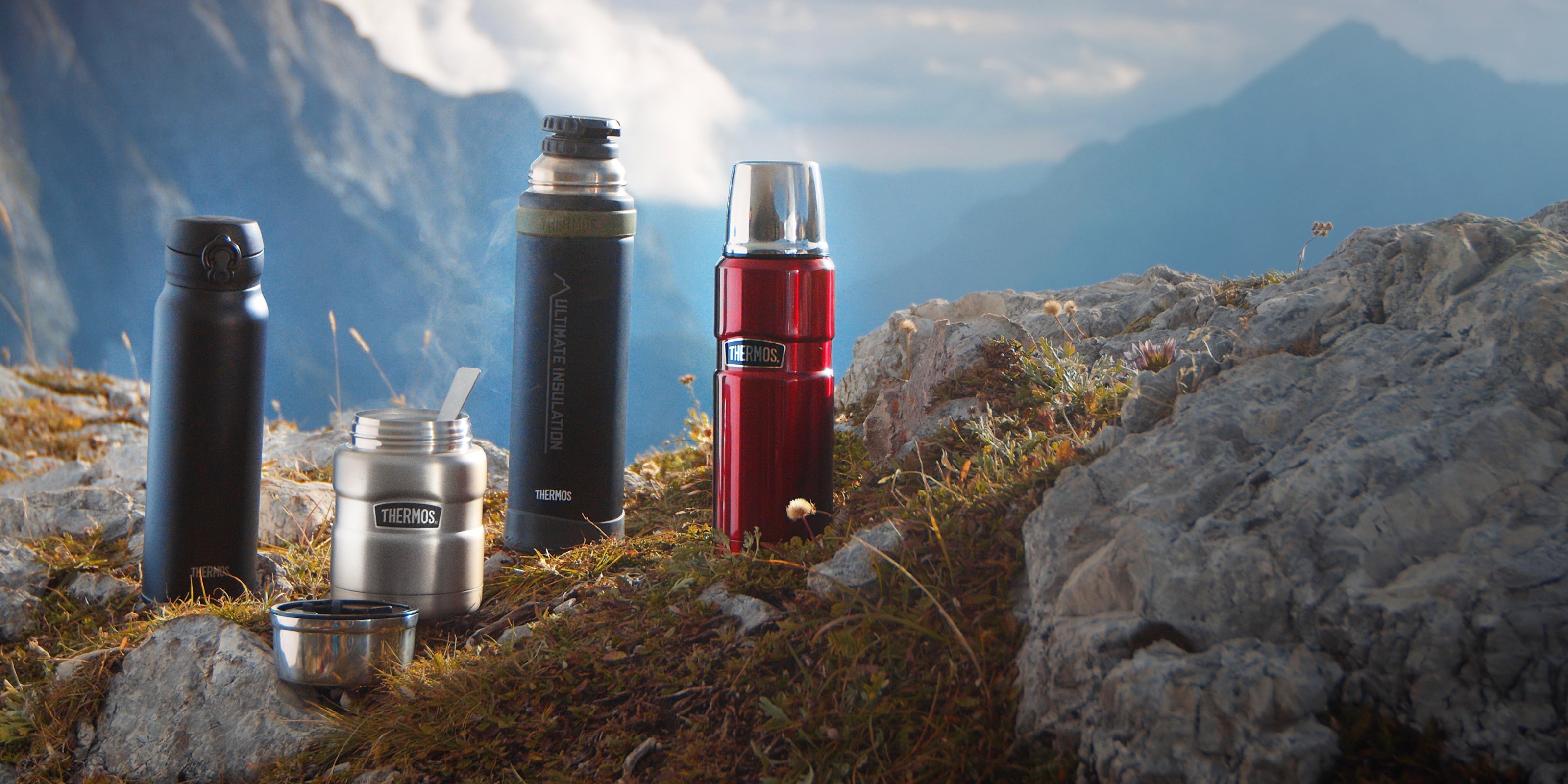 Verschiedene THERMOS Produkte auf einer Wiese mit Felsen und Bergen im Hintergrund
