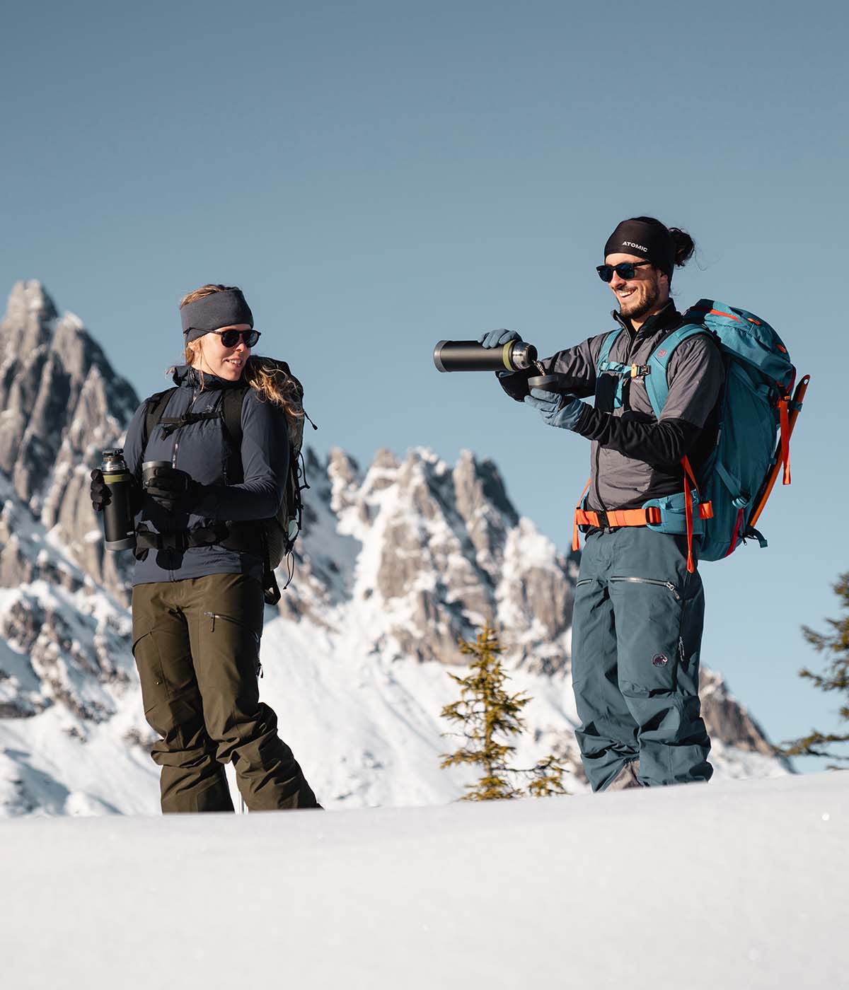Frau und Mann in den Bergen mit Ski und Thermosflaschen und Rucksäcken im Schnee