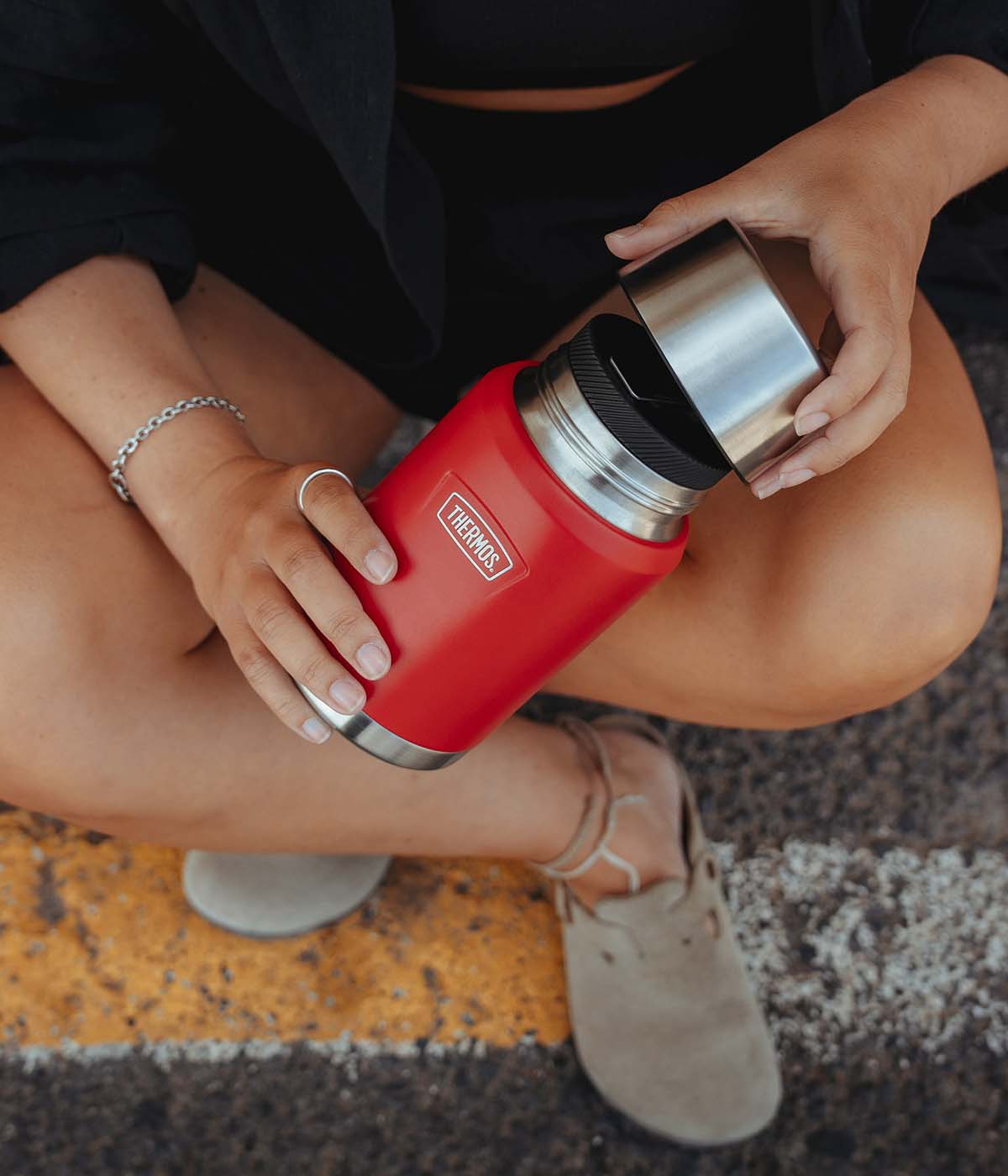 Nahaufnahme einer sitzenden Person, die einen roten THERMOS Thermobehälter mit silbernem Becher öffnet.