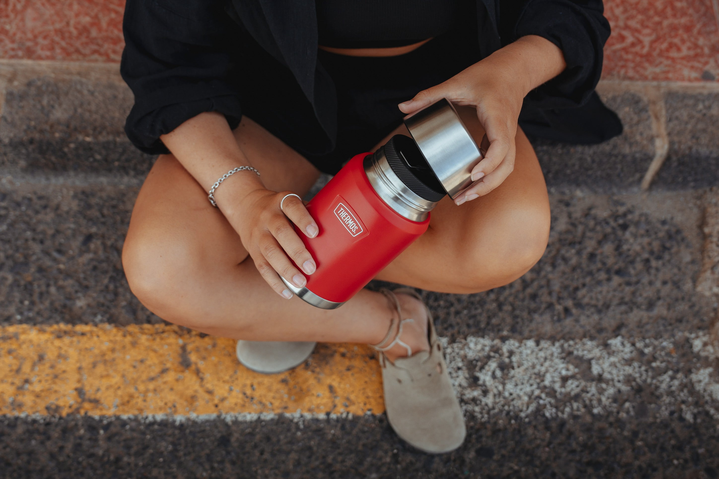Nahaufnahme einer sitzenden Person, die einen roten THERMOS Thermobehälter mit silbernem Becher öffnet.